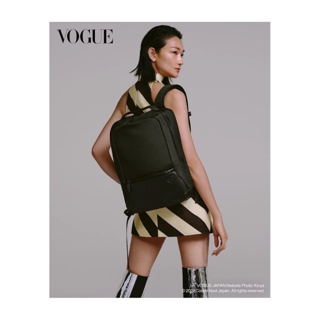 Asian woman poses with a black backpack in a studio setting, wearing a short striped dress and knee-high boots; Vogue logo visible.