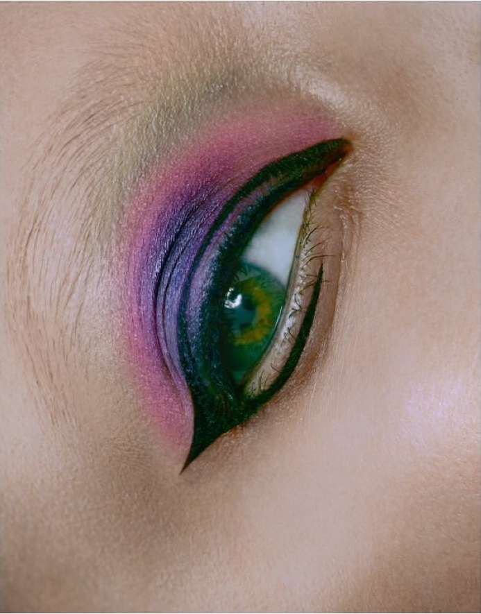 Close-up shot of a green eye with graphic purple and black eye makeup, capturing a bold beauty and cosmetic statement.