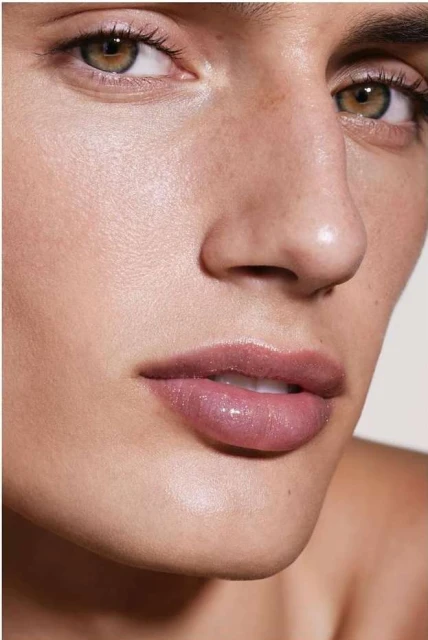 Close-up studio shot of a fair-skinned adult female with light brown hair, green eyes, freckles, and pink glossy lips.