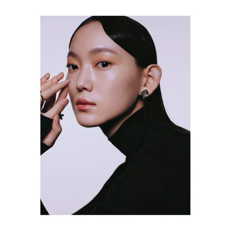 Close-up portrait of a woman wearing a black turtleneck and statement earrings against a plain background