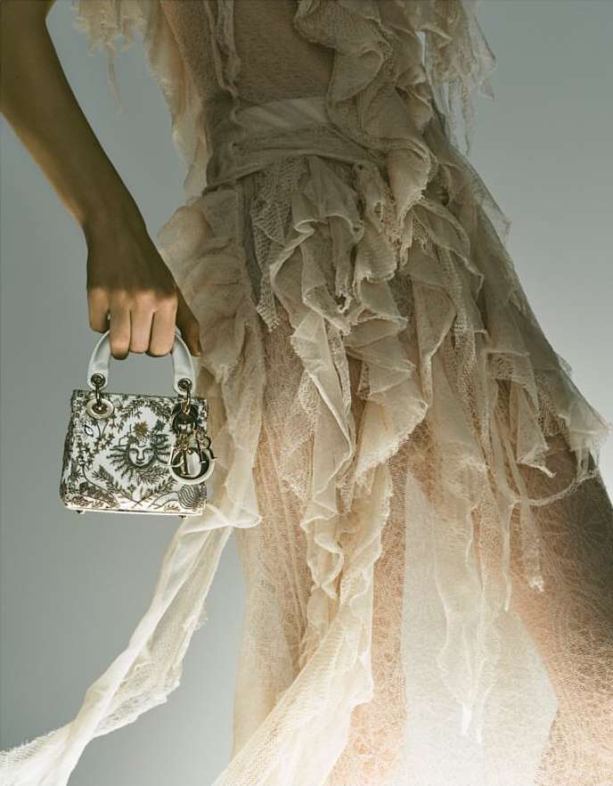 Elegant tulle dress with ruffles held by a woman's hand, accessorized with a designer handbag, for a fashion-forward and sophisticated style.
