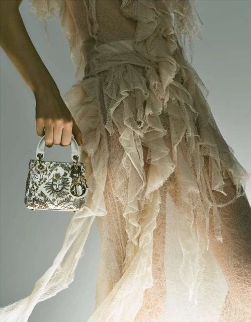 Elegant tulle dress with ruffles held by a woman's hand, accessorized with a designer handbag, for a fashion-forward and sophisticated style.