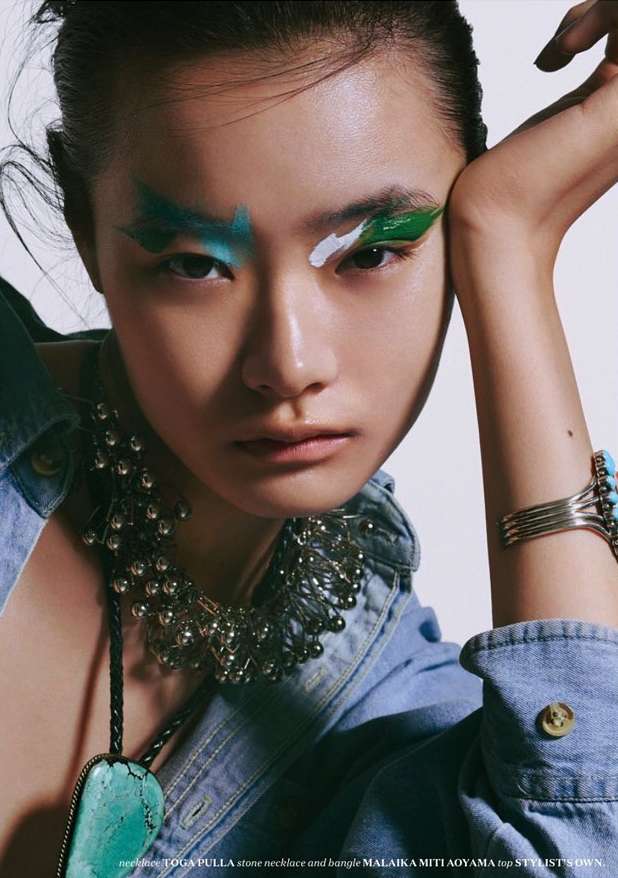 Asian woman with bold makeup and a denim jacket poses in a studio with silver jewelry. Beauty shot with fashion style.