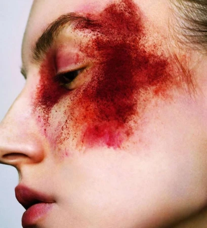 Close-up profile of a model's face with dramatic red pigment powder smeared across the eye and cheek.