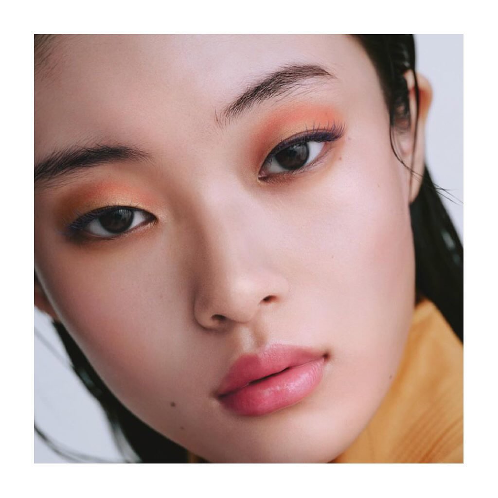 Close-up portrait of a woman with vibrant orange eyeshadow and pink lips against a plain white background