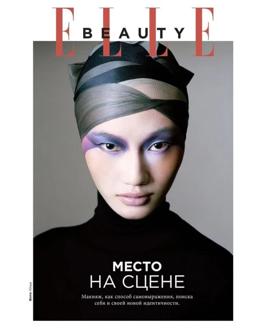 Elle Beauty magazine cover featuring a woman with creative makeup and a head wrap, set against a grey backdrop with bold typography.