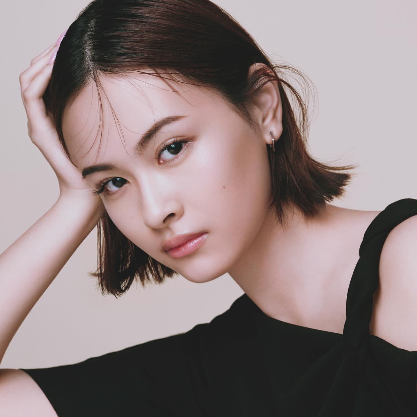 Portrait of a young woman with short brown hair and black top in studio lighting. She is resting her head on her hand.