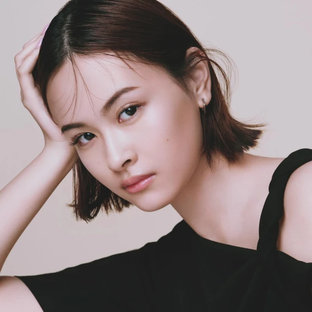 Portrait of a young woman with short brown hair and black top in studio lighting. She is resting her head on her hand.
