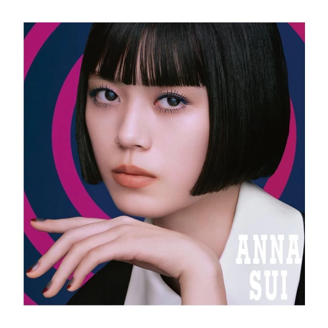 Close-up shot of an Asian female model with dark, short hair. Fashion portrait with graphic pink and blue background, 'ANNA SUI' text visible.