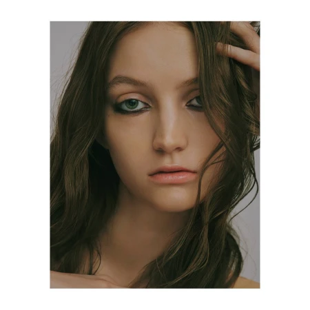 Close-up portrait of a young woman with dark hair, green eyes, and dramatic eyeliner against a neutral backdrop.