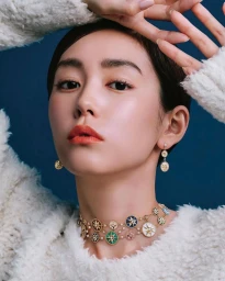 Close-up portrait of a woman wearing a gold star choker necklace and dangling earrings against a deep blue background.