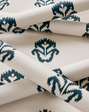 Rolls of wallpaper with a geometric teardrop pattern in dark teal on a cream background, creating a visually appealing texture.