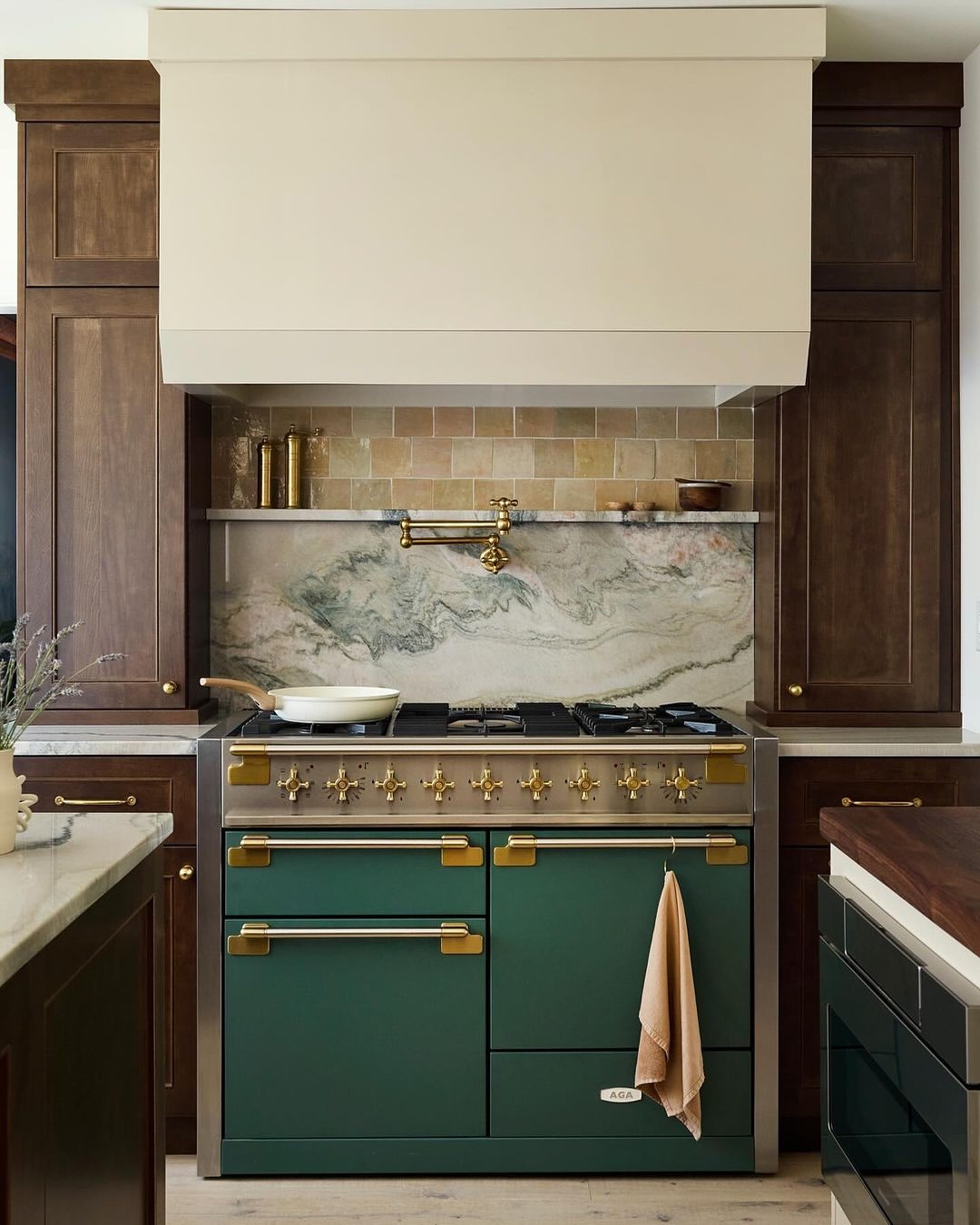 A modern kitchen features a green range cooker, set against a backsplash of marble and tan tile, complemented by dark wood cabinetry.