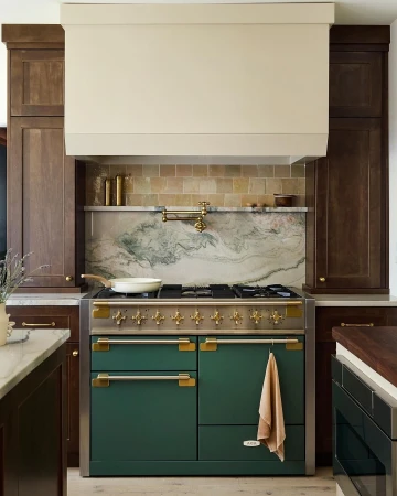 A modern kitchen features a green range cooker, set against a backsplash of marble and tan tile, complemented by dark wood cabinetry.