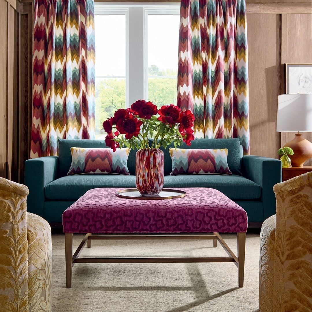 Living room interior featuring a teal couch, patterned ottoman, and vibrant floral arrangement in a decorative vase on a metal tray.