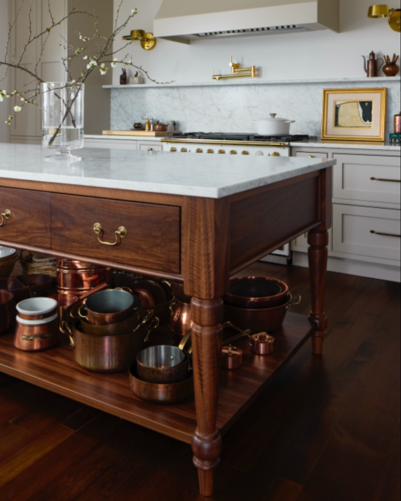 Kitchen interior with a wood island, marble countertop, copper pots, and white cabinets, creating a warm, traditional culinary space.