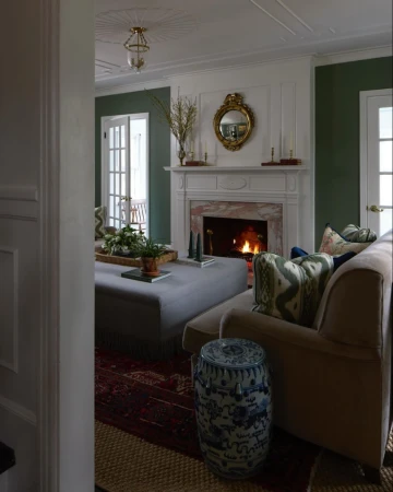 Living room interior with a fireplace, ottoman, sofa, and garden stool, showcasing a cozy and inviting home decor setting.