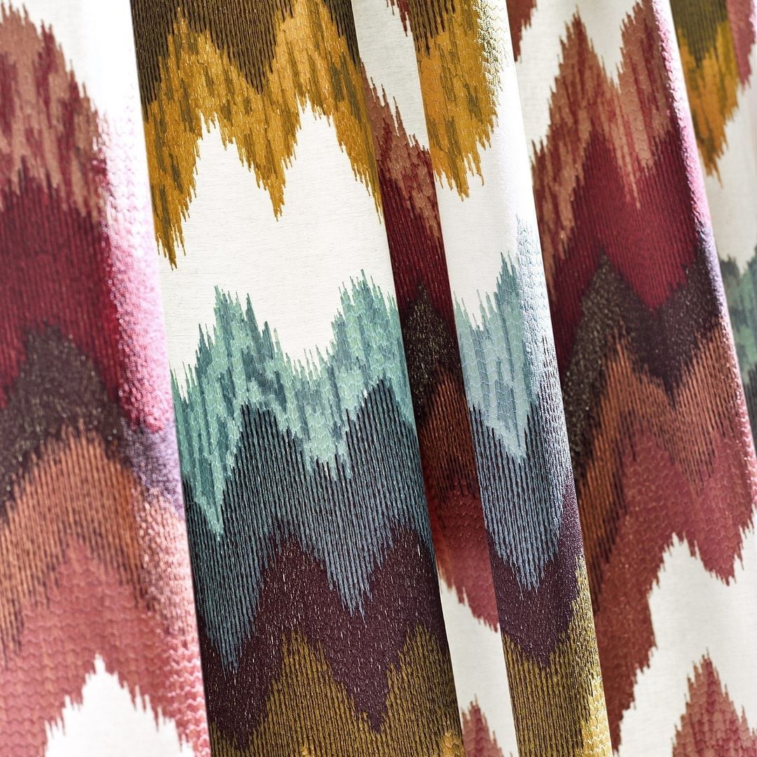 Close-up of a textile featuring a colorful zigzag pattern in hues of red, yellow, blue, and brown on a light background, fabric texture.