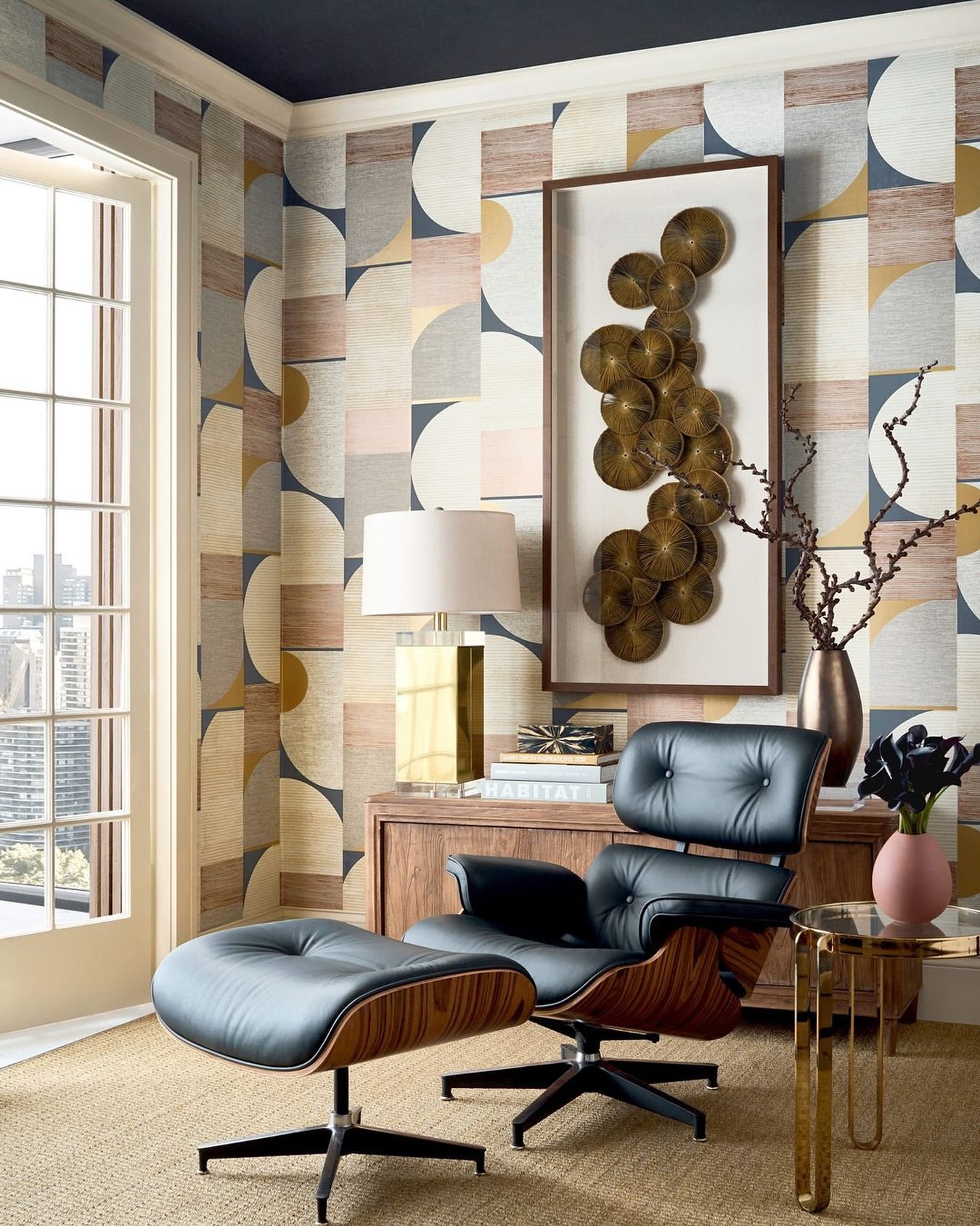 Modern interior with a black leather lounge chair and ottoman set against patterned wallpaper and a window view of the city skyline.