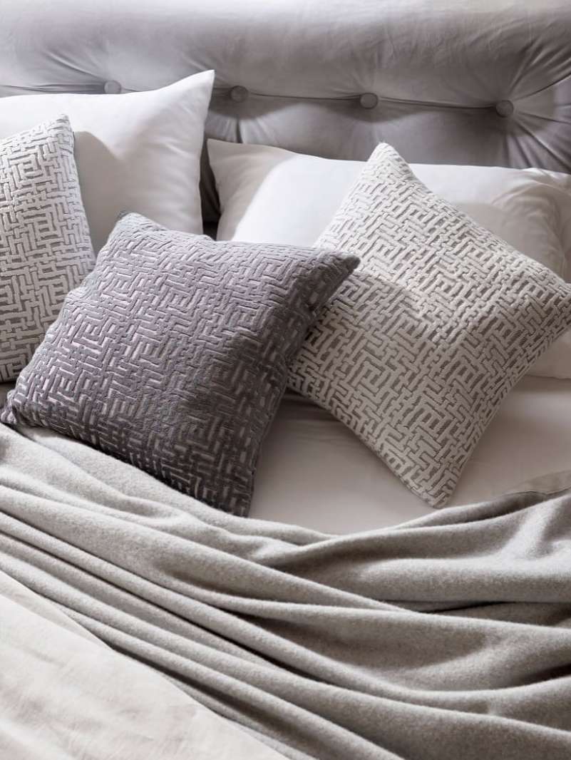 Arrangement of textured pillows and a soft, light gray blanket on a bed with a tufted headboard creates a cozy and inviting bedroom scene.