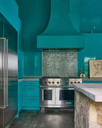 Glossy teal kitchen with stainless steel range oven and tiled backsplash photographed by Kip Dawkins