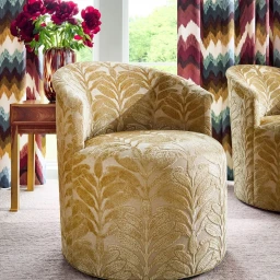 Textured gold leaf pattern armchair in a bright living room with patterned drapes and red flowers in a vase.