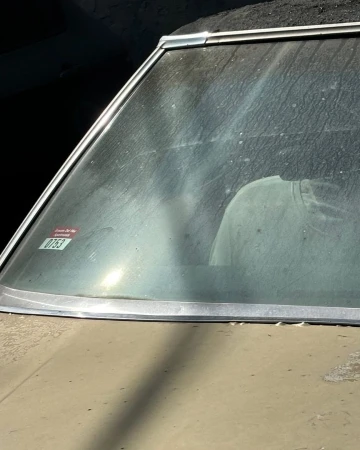 Close-up of a tan vintage car with a dirty windshield reflecting a white object, possibly a shirt, against a dark background.