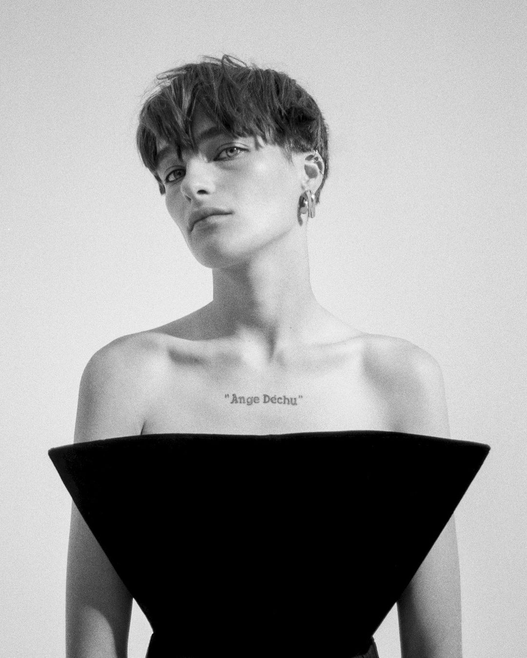 Striking black and white portrait of an adult woman with short hair wearing a modern black top against a white backdrop.