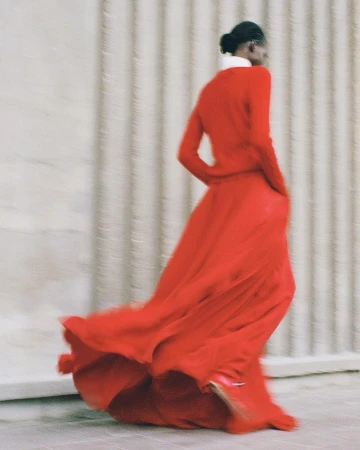 Model in vibrant red dress captured in motion against a structured fluted wall in Paris by Kira Bunse