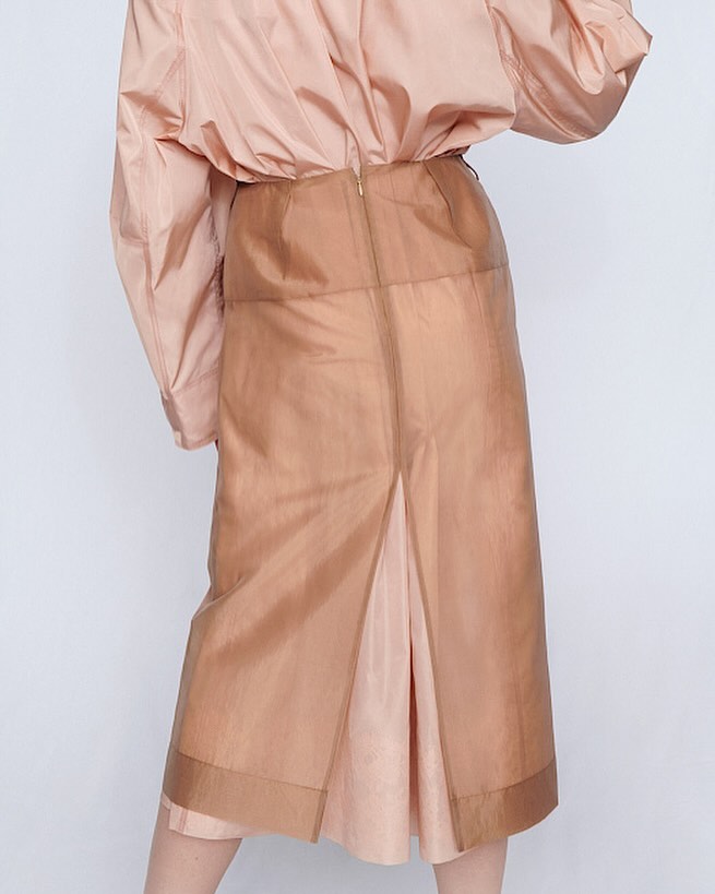 Pale peach semi-sheer midi skirt with a slit, styled with a matching button-down top, isolated on a plain background for fashion editorial.