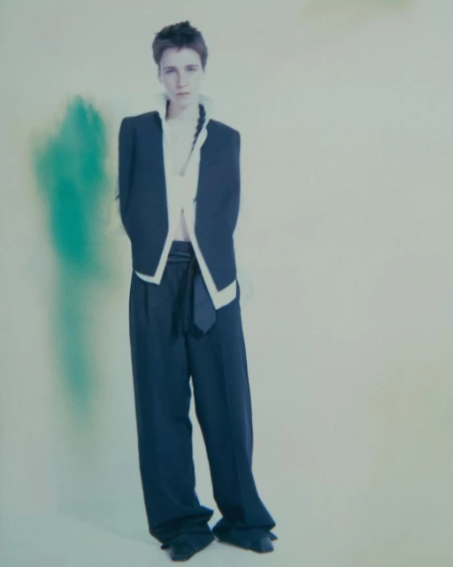 Fashion portrait of a woman in a navy jacket and wide-leg pants against an abstract off-white and green background in studio lighting.