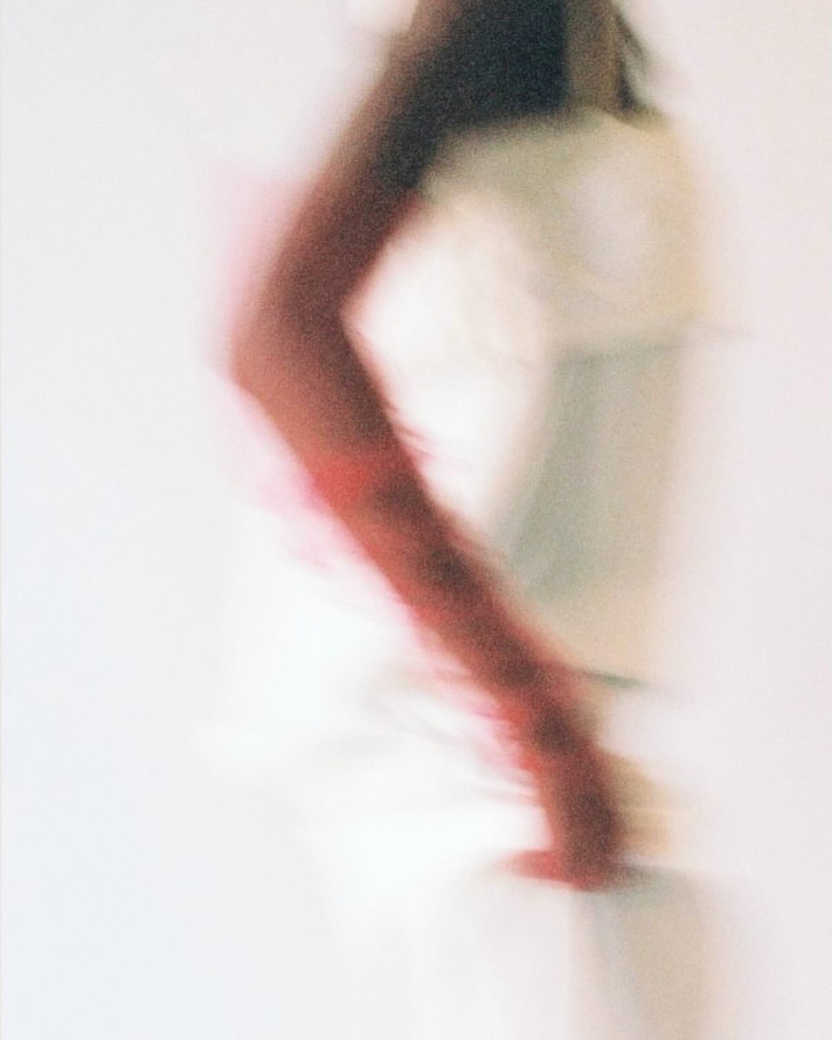 Motion blurred photographic portrait of a person wearing a red sleeve against a plain white background