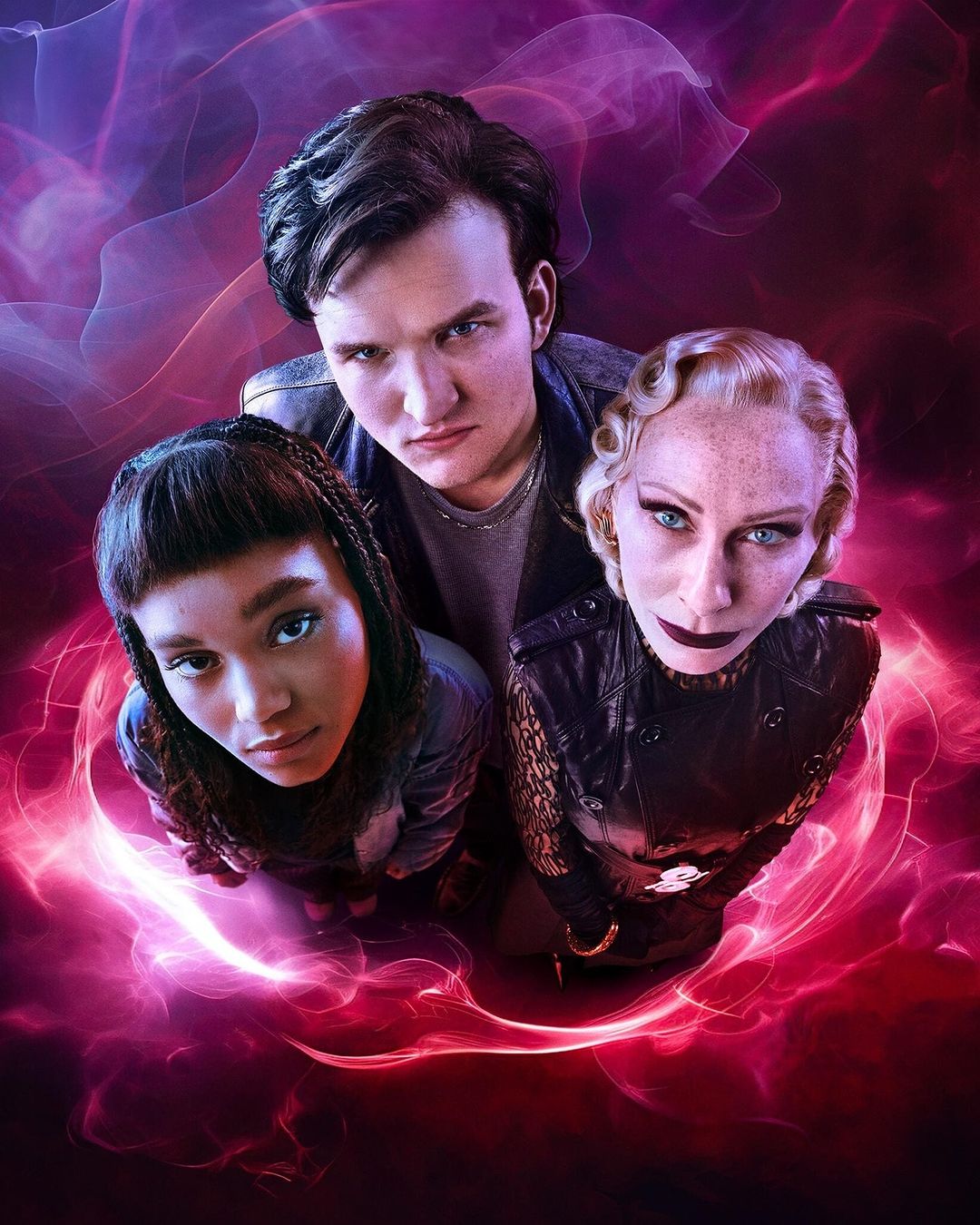 Three people – an adult female, an adult male, and a young female – pose together in a low-angle shot with a dramatic purple and red backdrop.