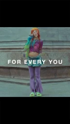 Woman with long orange hair wearing a colorful top and purple pants standing in front of stone architecture