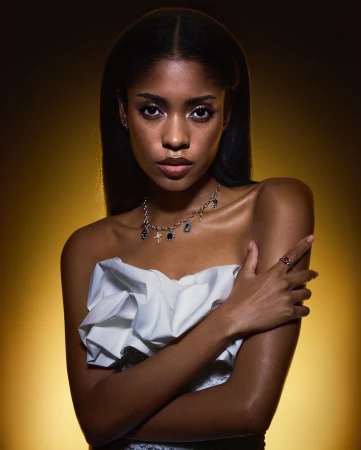 Portrait of a Black woman wearing a white ruffled top and silver charm necklace against a warm yellow gradient background.