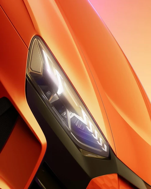 Close-up shot of the front headlight of an orange sportscar, highlighting its design and texture in a studio setting.