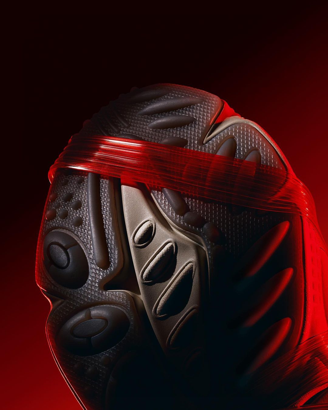 Close-up studio shot of the upper and toe portion of a soccer shoe with textured surface and red elastic band against a red backdrop.