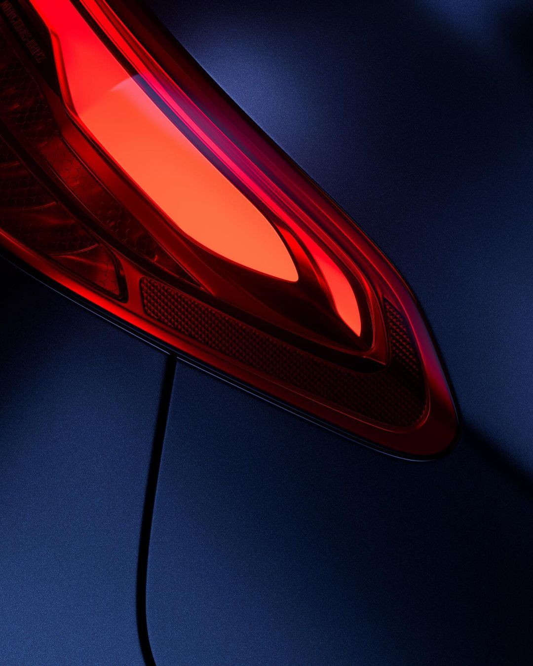 Close-up of a blue car's glowing red taillight with a modern design, reflecting light and shadows in a dark, automotive setting.