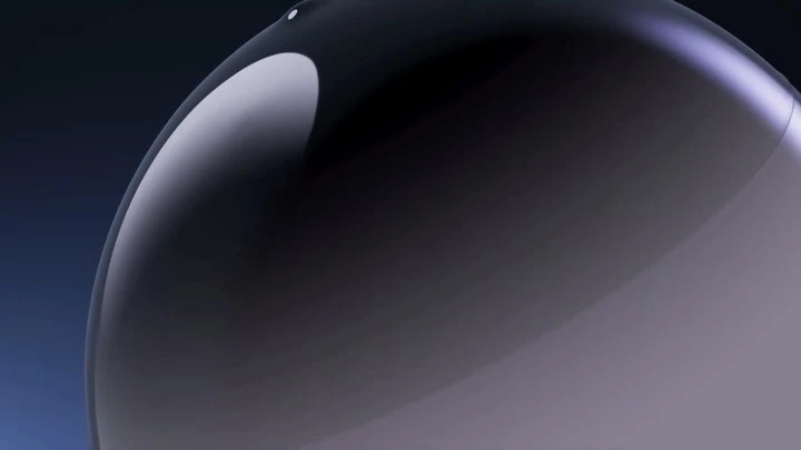 Close-up studio shot of a glossy, semi-translucent, dome-shaped object with gradient color shifts on a dark blue background.