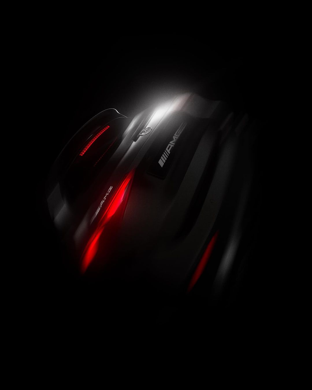 Sleek black sports car, an AMG model, dramatically lit with vibrant red accents against a dark background showcasing automotive design.