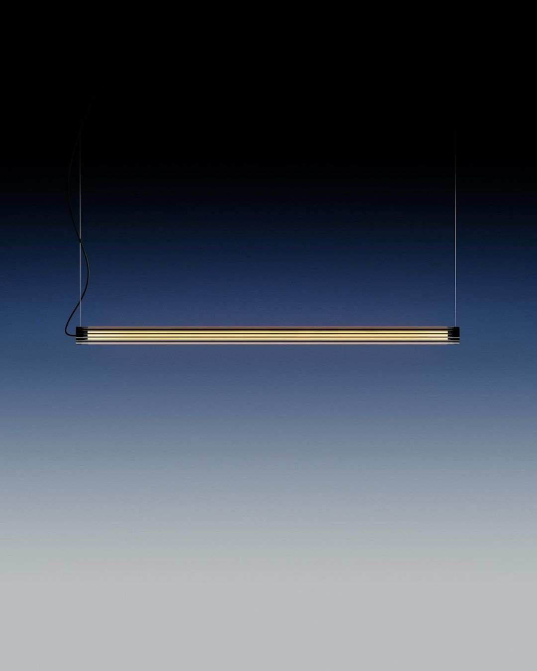 Minimalist black linear suspension light fixture with a diffused golden light element against a dark blue to grey gradient background.