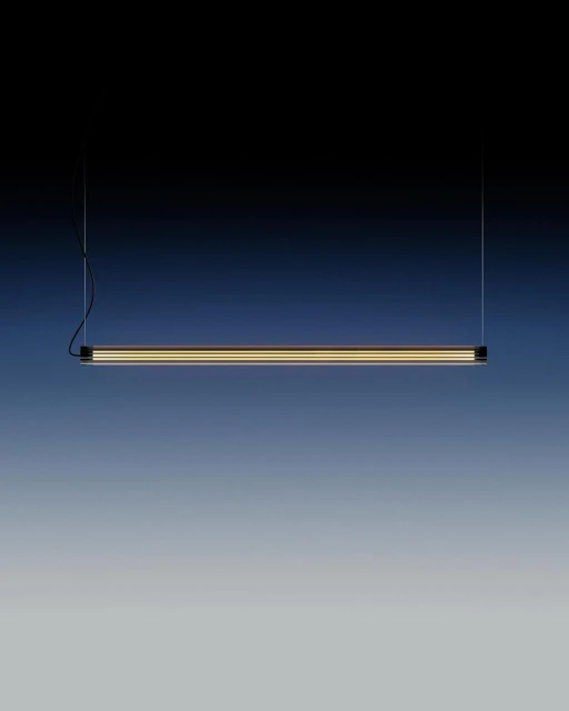 Minimalist black linear suspension light fixture with a diffused golden light element against a dark blue to grey gradient background.