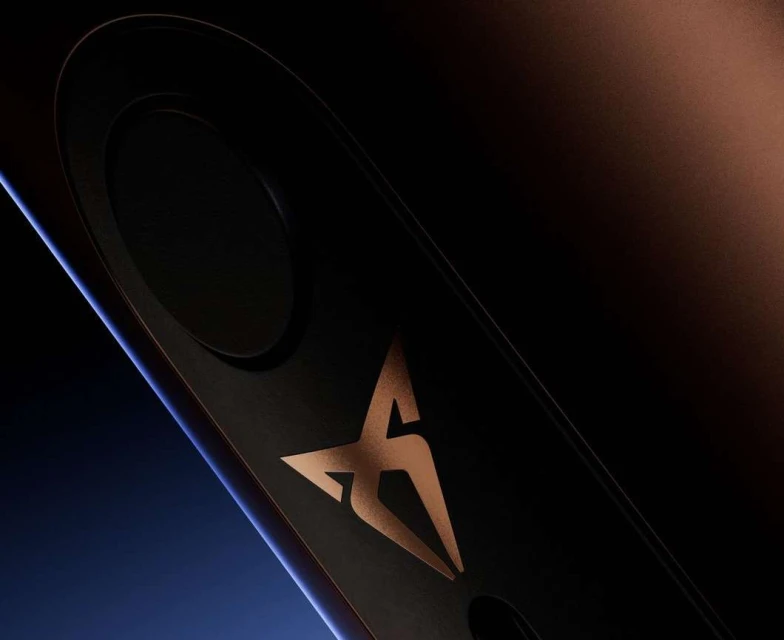 Close-up of a black automotive part with a copper-colored logo, displaying sleek design and modern aesthetics against a dark background.