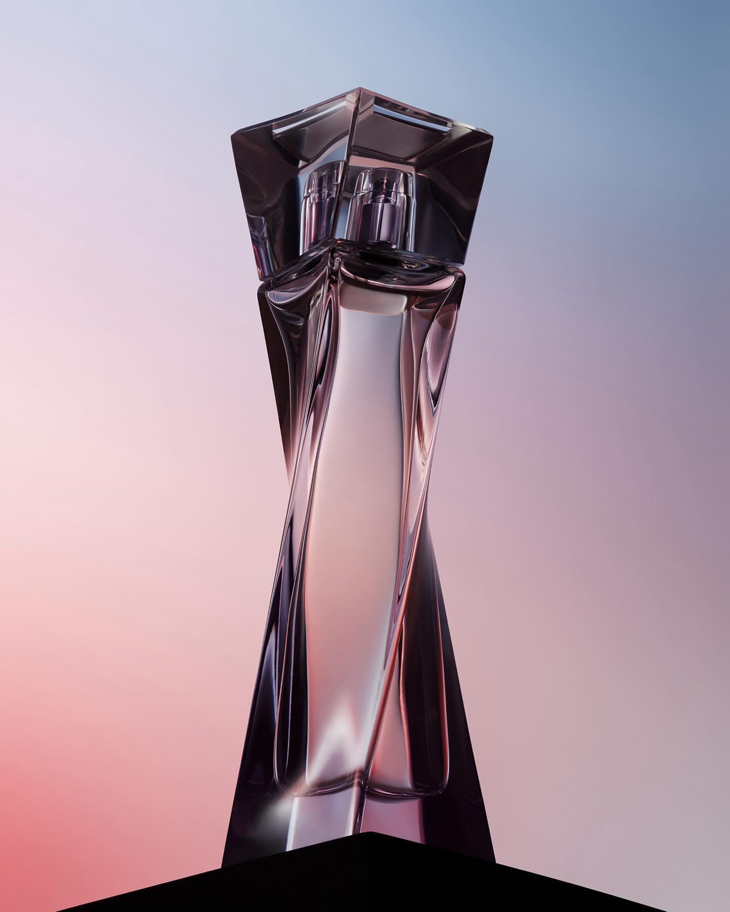 Sleek and modern crystal perfume bottle with a geometric design against a soft gradient background of pink, purple, and blue.