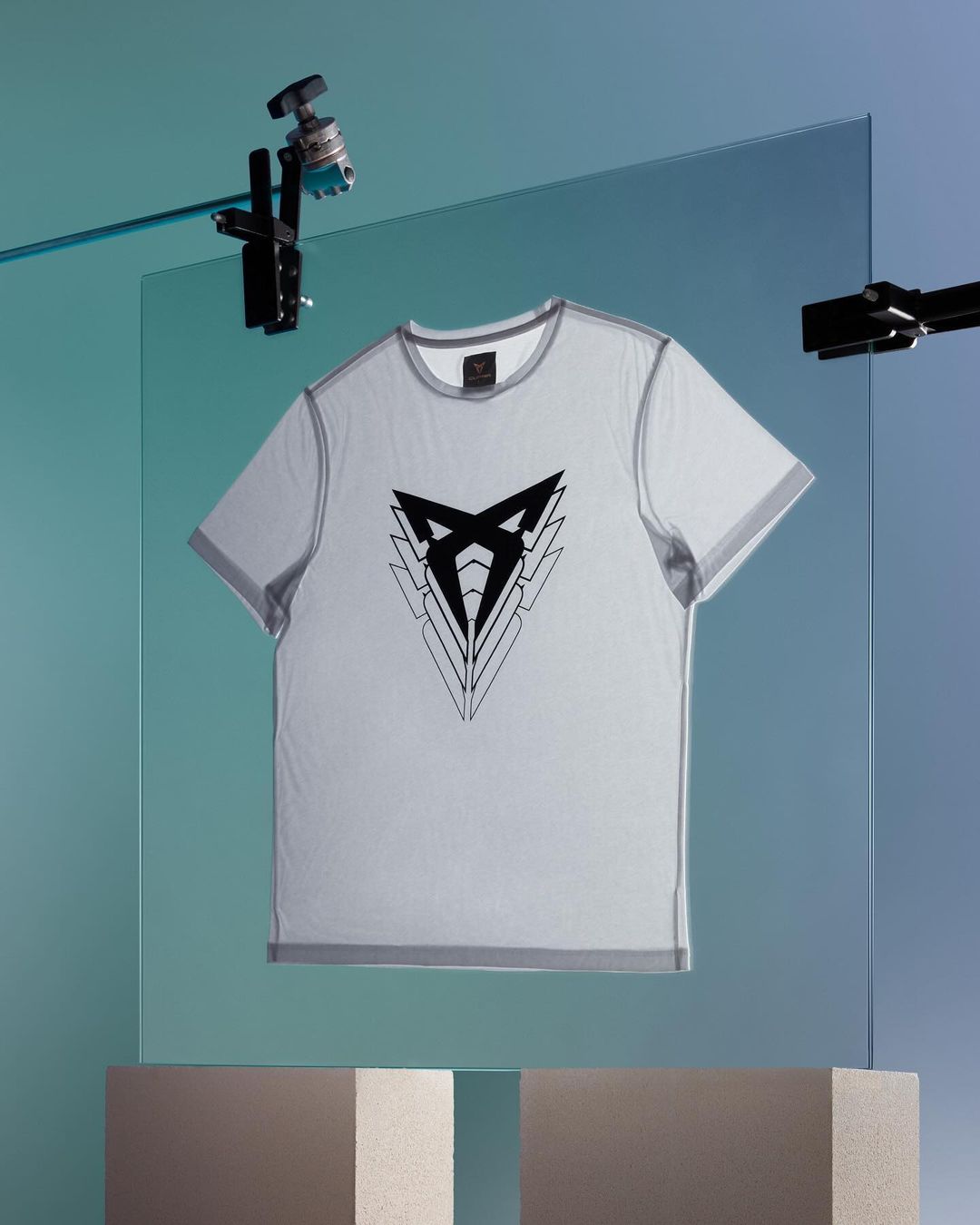 White t-shirt with a geometric logo, suspended in a studio setting against a gradient blue background, lit by studio lighting.