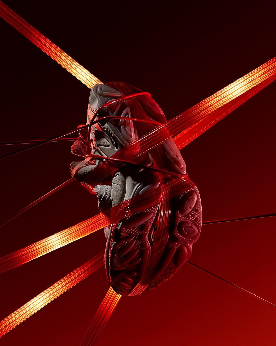 Grey athletic sneaker suspended in air and wrapped with bright red luminous ribbons against a deep red background.