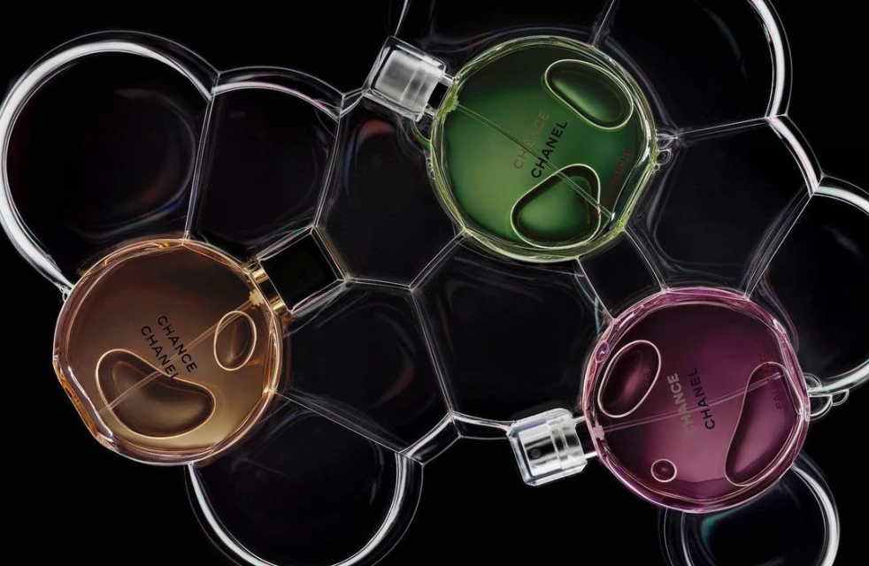 A studio shot of three Chanel Chance perfume bottles in amber, green, and pink, surrounded by transparent bubble shapes on a black backdrop.