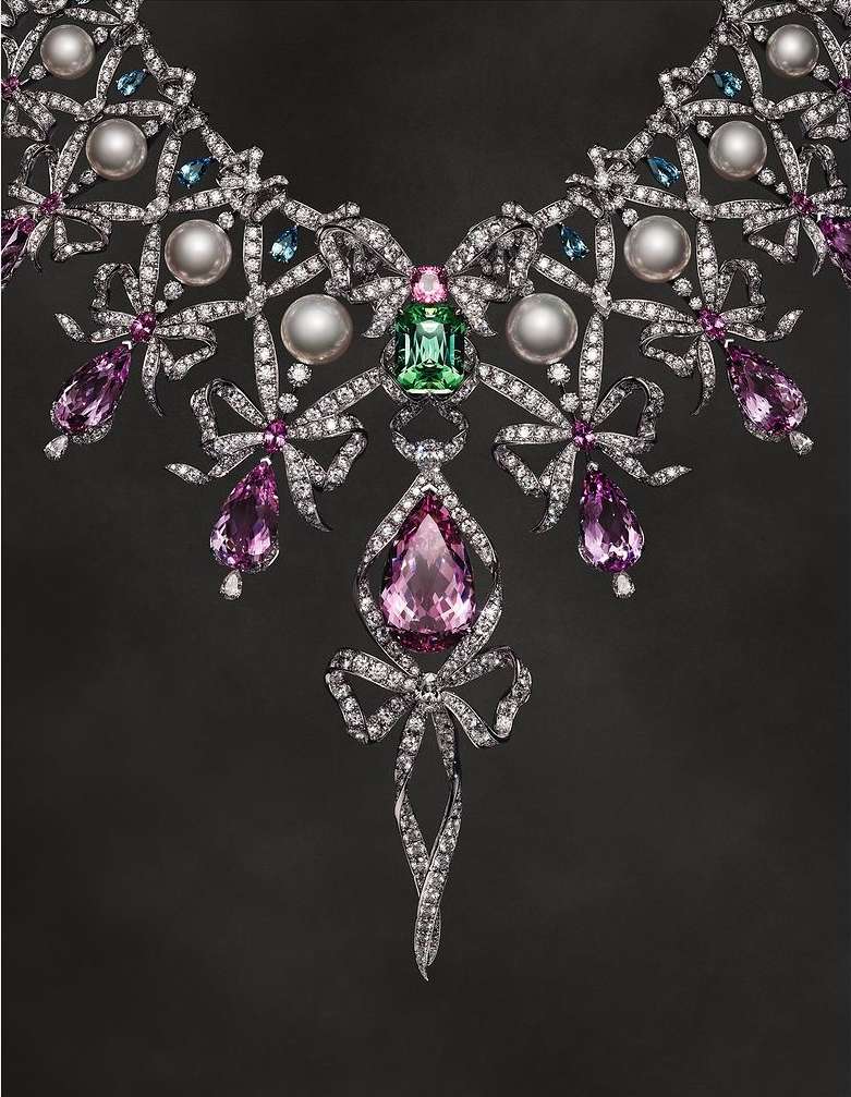Exquisite jeweled necklace featuring diamonds, pearls, and colored gems in a bow design on a dark background. Jewelry, diamonds, gems.