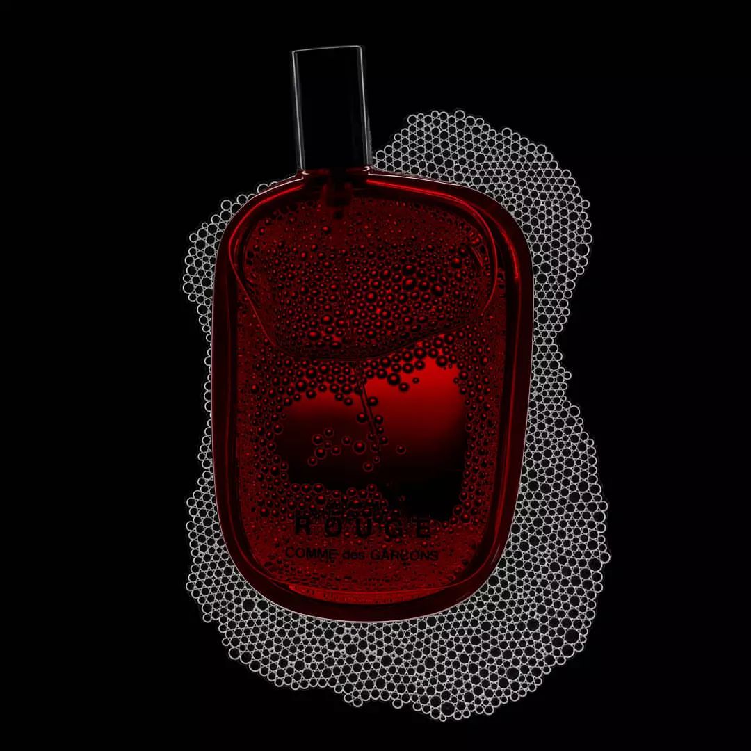High-contrast still life of a red perfume bottle by Comme des Garçons surrounded by foam bubbles against a stark black background.