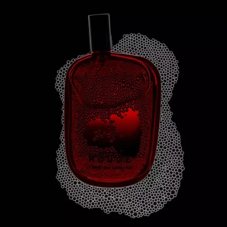 High-contrast still life of a red perfume bottle by Comme des Garçons surrounded by foam bubbles against a stark black background.